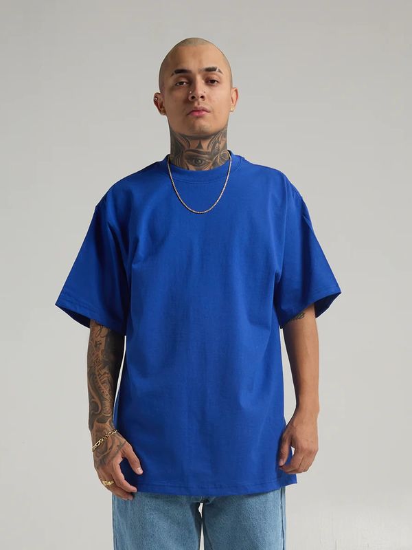 Man with tattoos wearing a blue oversized t-shirt and light blue jeans.