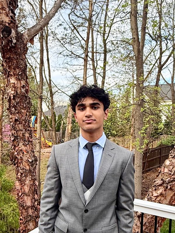 Young man in a grey suit and black tie standing outdoors.