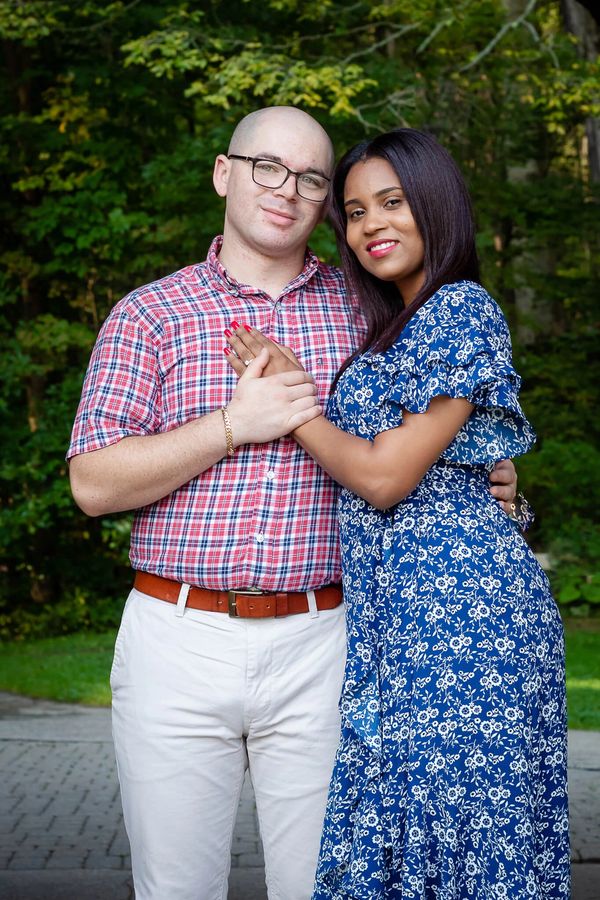 A couple stands outdoors, smiling at the camera, with their arms around each other.