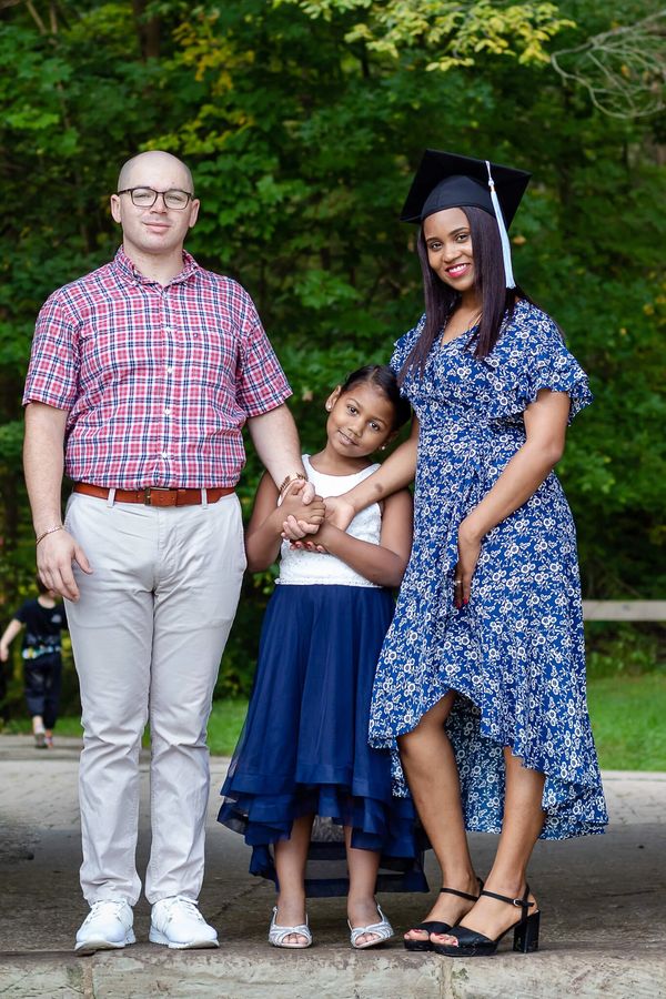 Family of three: man in plaid shirt, girl in blue dress, woman in graduation cap and dress.