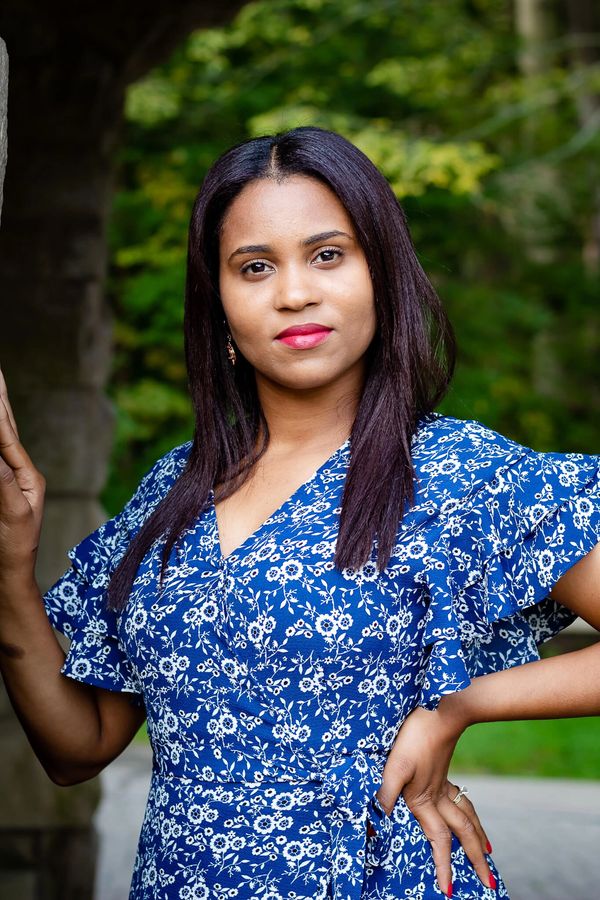 A woman in a blue floral dress posing confidently outdoors near stone architecture.