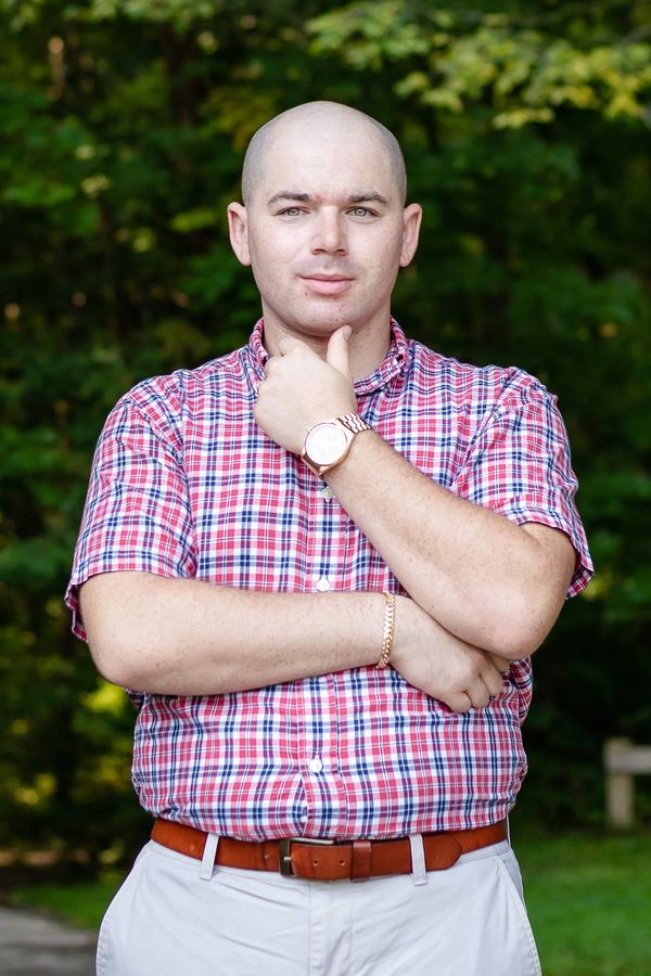 A man in a red plaid shirt standing confidently outdoors.