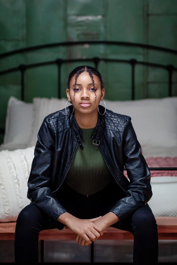 Young woman indoors, in a black leather jacket and hoop earrings, with a confident expression.