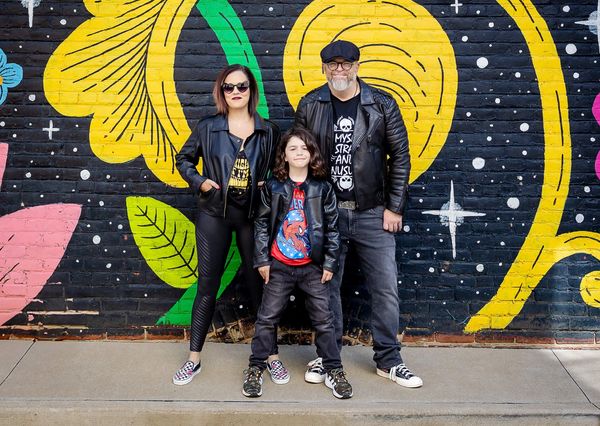 Family of three posing in front of a colorful mural.