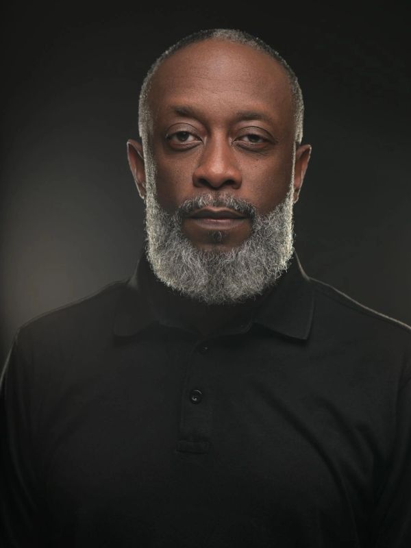 Portrait of a serious man with a gray beard wearing a black shirt.