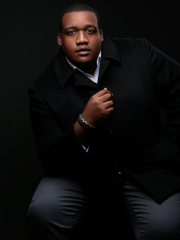 Portrait of a man in dark clothing against a black background.
