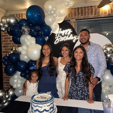 A family of 5 posing celebrating their daughter’s quinceanera in front of her birthday cake.