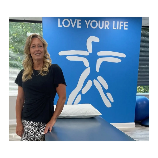 Woman standing next to a therapy table with a motivational wall sign.