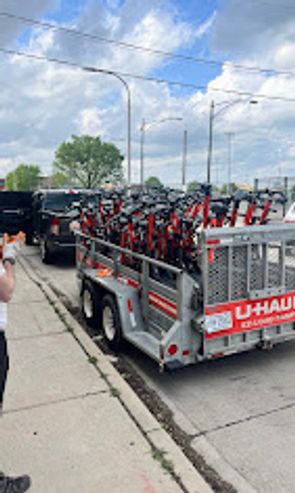 A U-Haul trailer loaded with many red rental scooters on a city street.