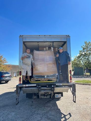Two men giving thumbs up in the back of a truck with a large pallet.