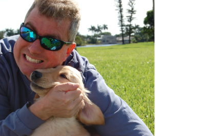 Man smiling with dog outdoors on grass.
