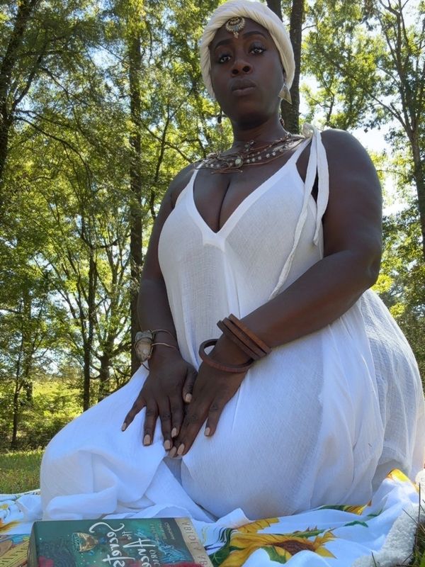 Woman in white dress sitting on a blanket outdoors.