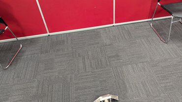 Carpet cleaning tool on a gray carpet with red walls and black chairs.