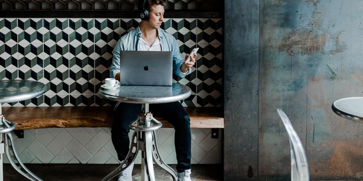 Man in cafe working on laptop and looking at phone.