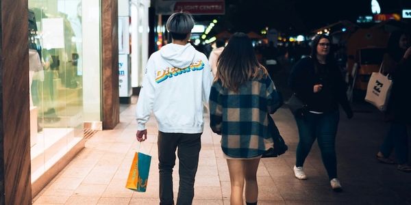 Two people walking together at night in a shopping area.