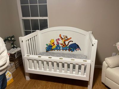 White baby crib with Winnie the Pooh characters painted on the headboard.