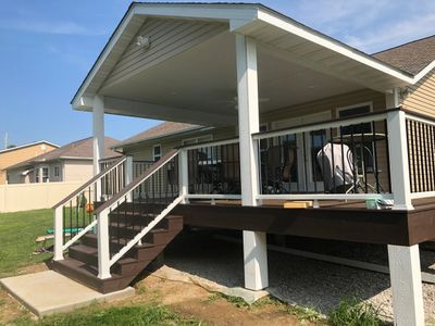 Covered porch with stairs and railing on a sunny day.