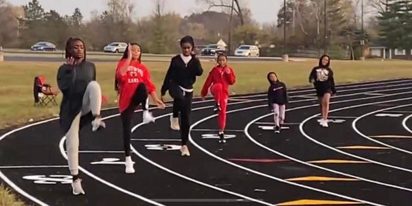 Six girls exercising on a track, lifting legs in sync.