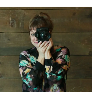 Woman in floral blouse taking a photo with a camera.