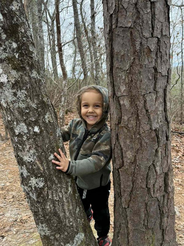 Smiling child between two trees in a forest.