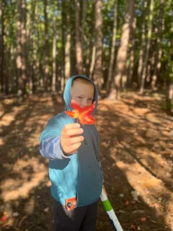 Child in hoodie holding a red autumn leaf.