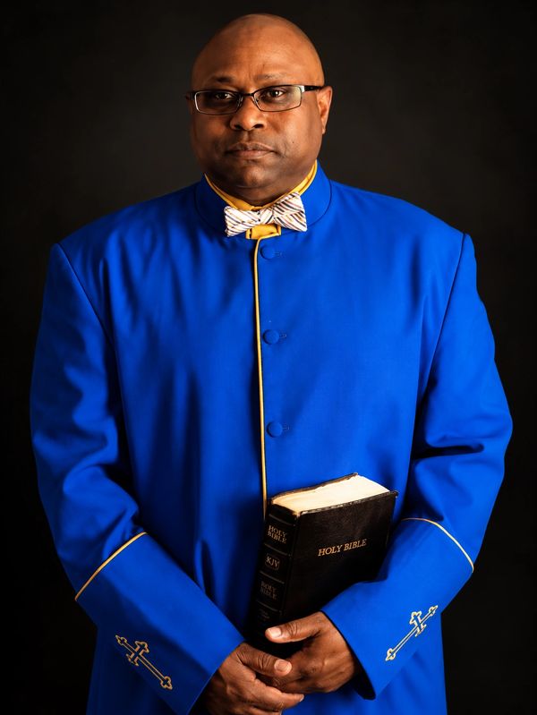 Man in blue clergy robe holding a Holy Bible.