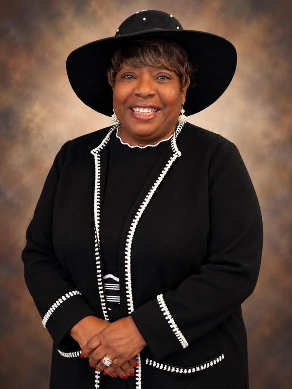 Smiling woman in black outfit and wide-brimmed hat.