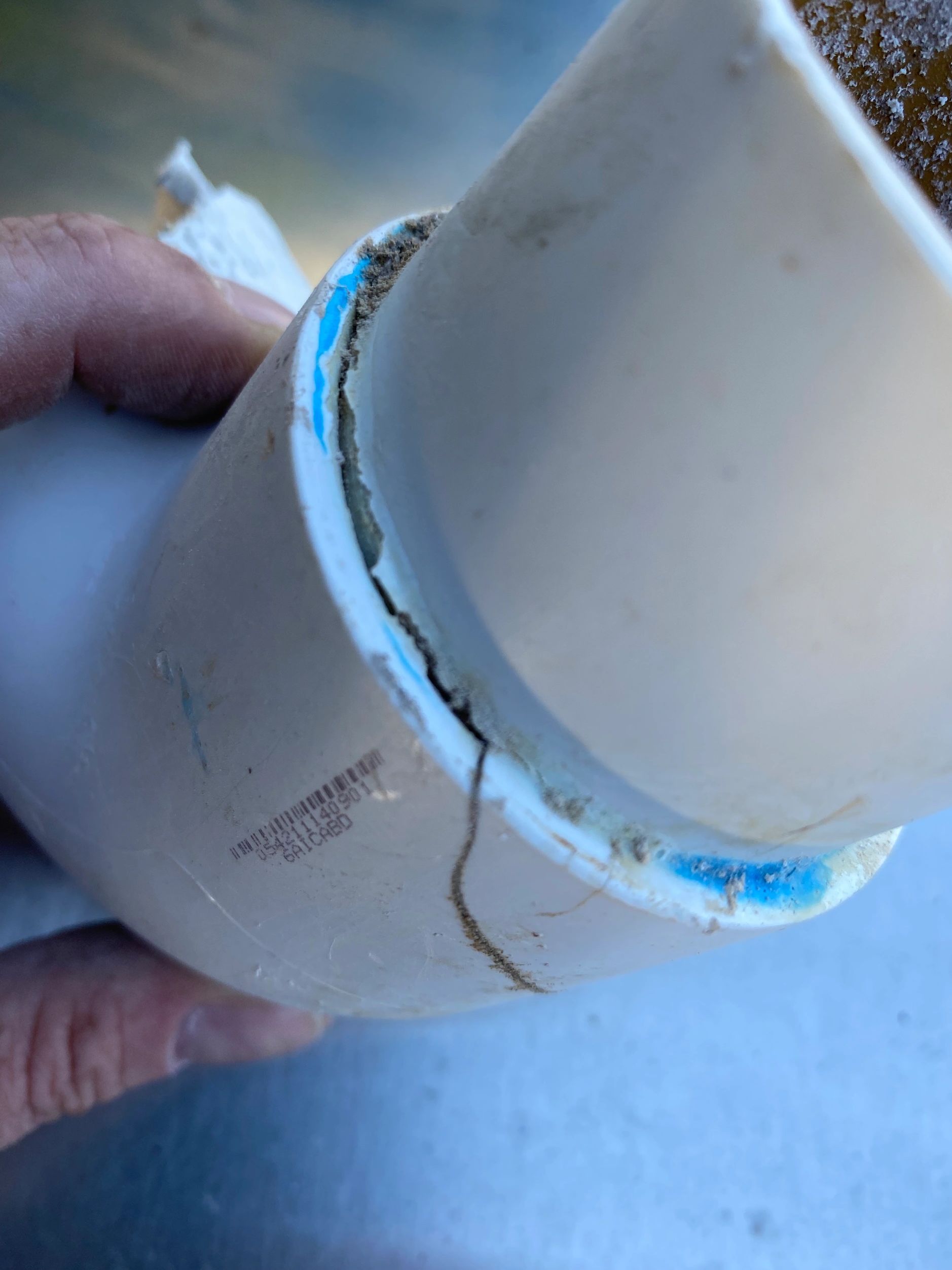 Close-up of a cracked white PVC pipe joint with dirt and debris.
