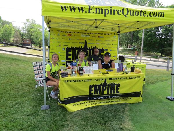 Four people sitting behind a table and under a canopy with the Empire Insurance logo on it.
