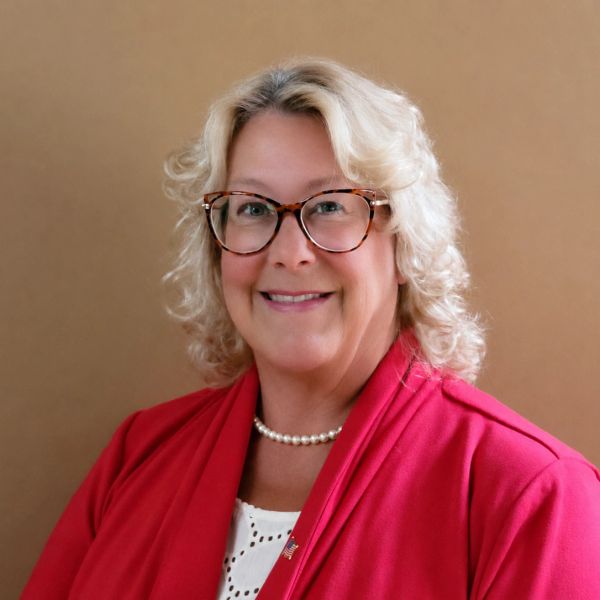 Smiling woman with glasses in red attire against brown background.