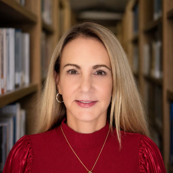 Woman with blonde hair in a red top standing in a library.