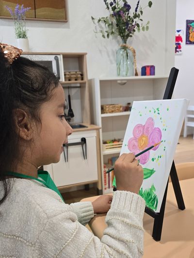 A girl painting a pink and yellow flower on canvas.