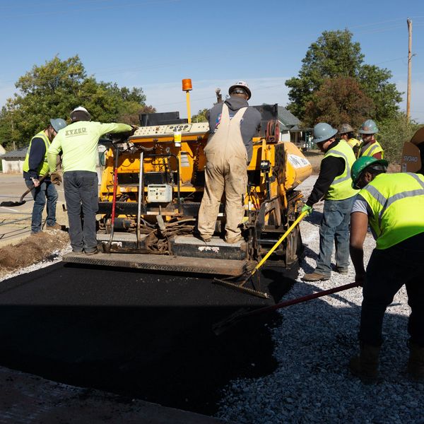 Workers paving a road with heavy machinery on a sunny day.