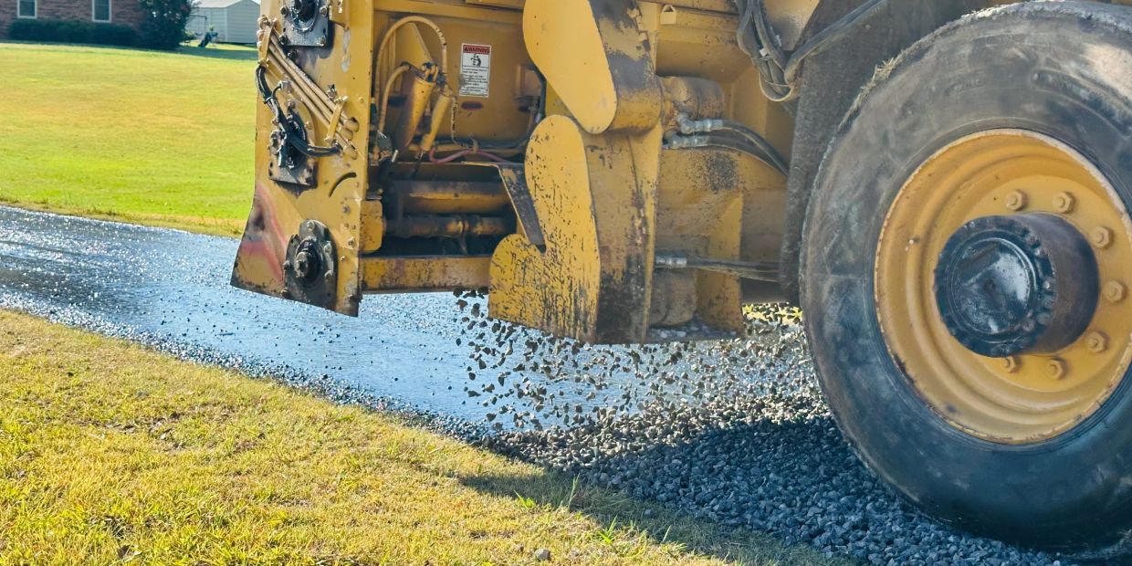 Yellow construction vehicle spreading gravel on a road.