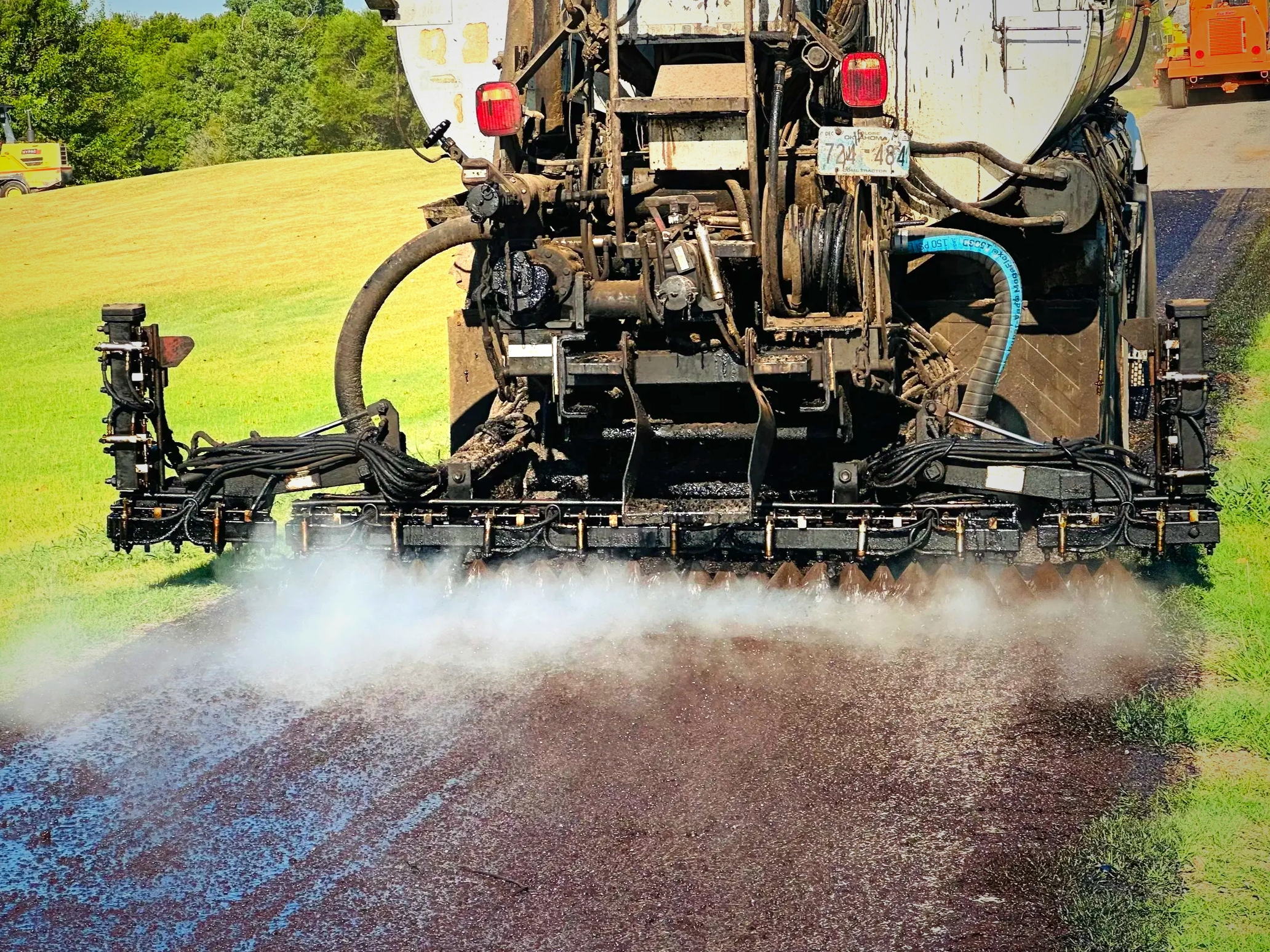 Road construction vehicle spraying asphalt on a rural road.