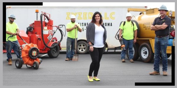 A woman stands confidently in front of four workers in safety gear and machinery.
