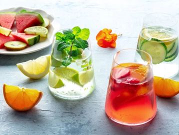 Colorful fruit-infused drinks with fresh fruit slices and mint on a light table.