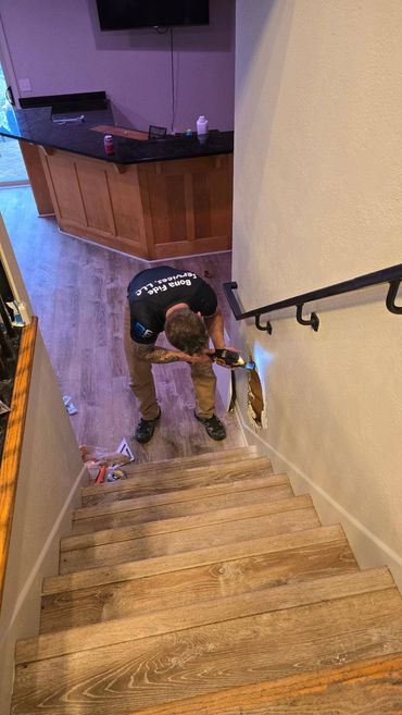 Sidney working on the damaged drywall beside the stairway and black handrail.