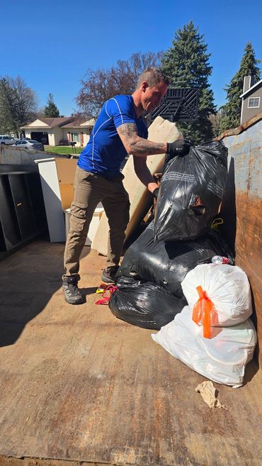 Sid loading bags and dismantled materials into a dumpster.
