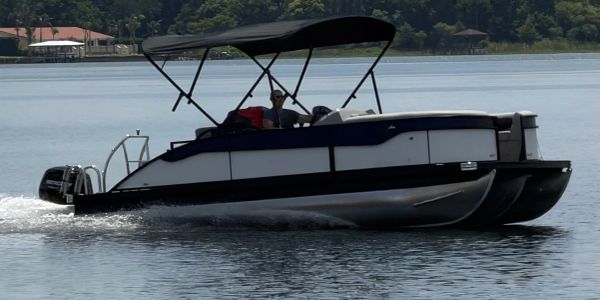 Person driving a black and white pontoon boat on calm water.