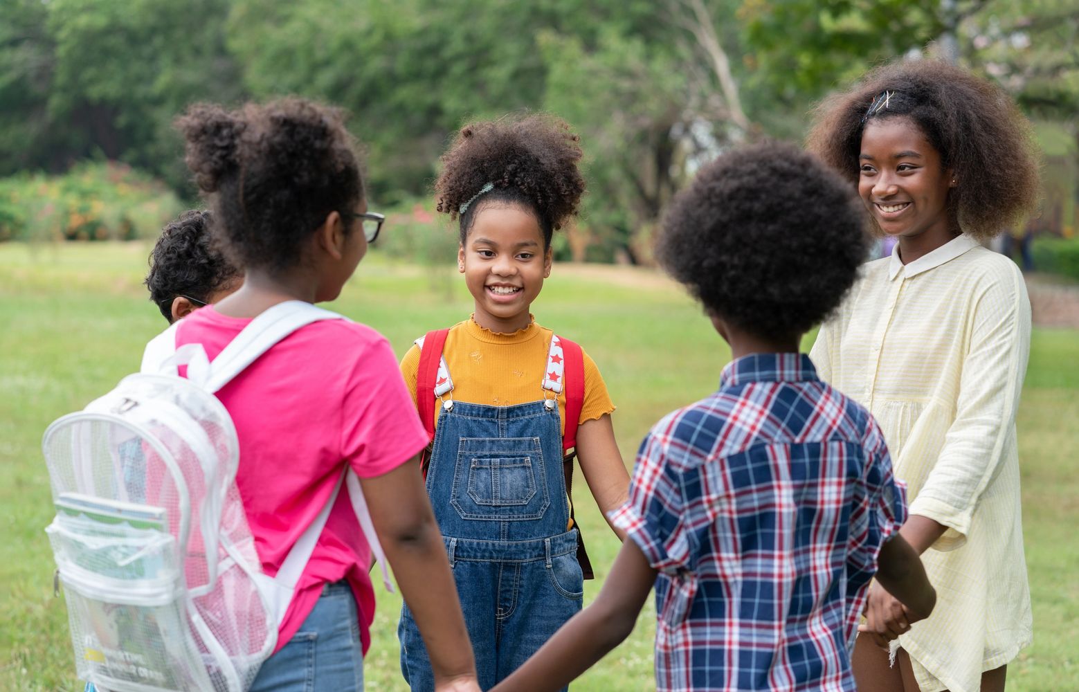A group of smiling black girls holding hands in a circle outdoors.