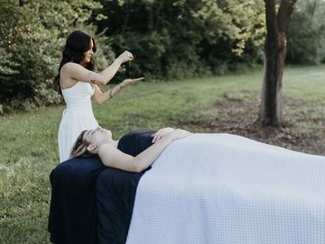 Woman giving a healing session to another woman outdoors.