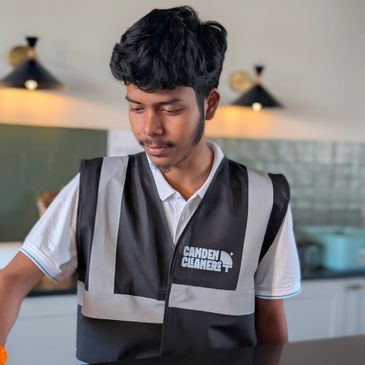 Young man in a Camden Cleaners vest cleaning a surface.