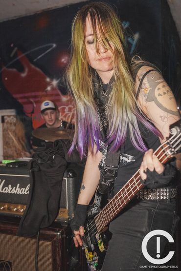 A woman with green and purple long hair wearing a black sleeveless t shirt and black jeans with a st