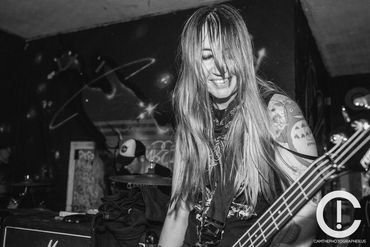 Black and White photo of a woman with light long hair plays bass against a graffiti wall background.
