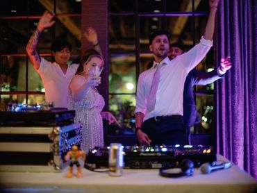 Guests dancing with raised hands near the DJ booth during a lively evening reception.