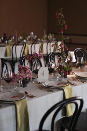 Elegant dinner table setting with orchids, wine glasses, gold flatware, and soft candlelight.