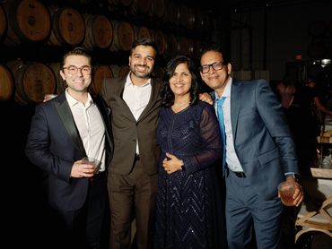 Four guests smiling and posing together with drinks at an elegant evening event inside a winery.