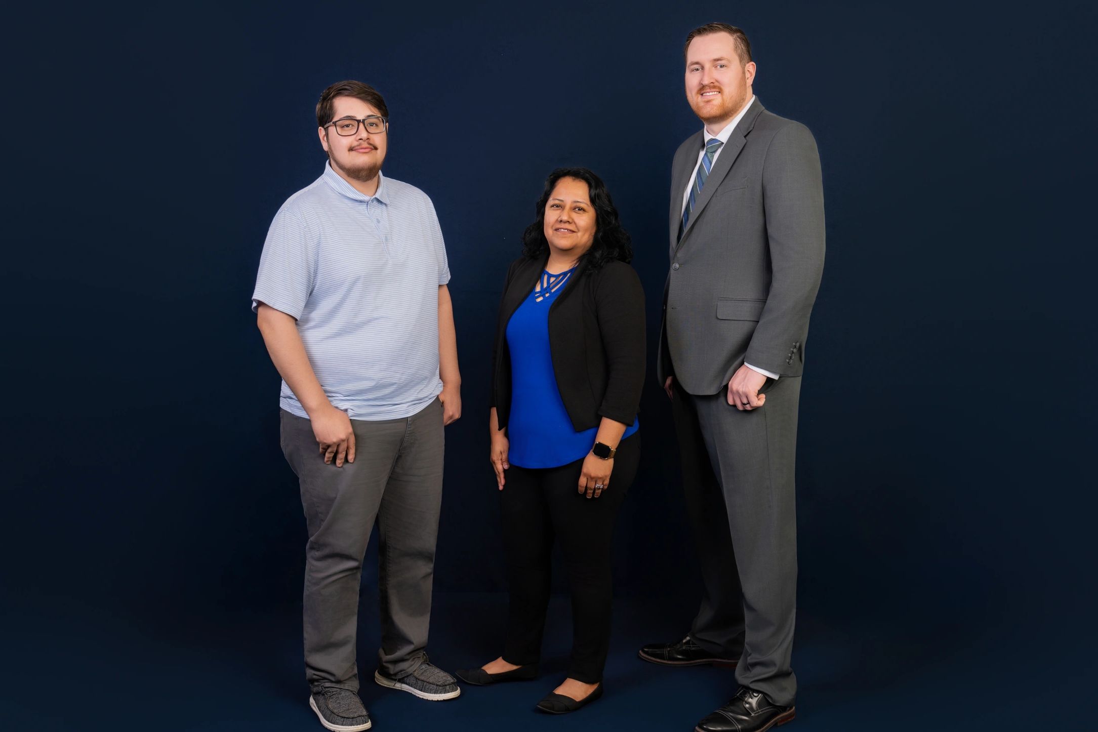 Three professionals posing against a dark blue backdrop, showing diverse business attire.