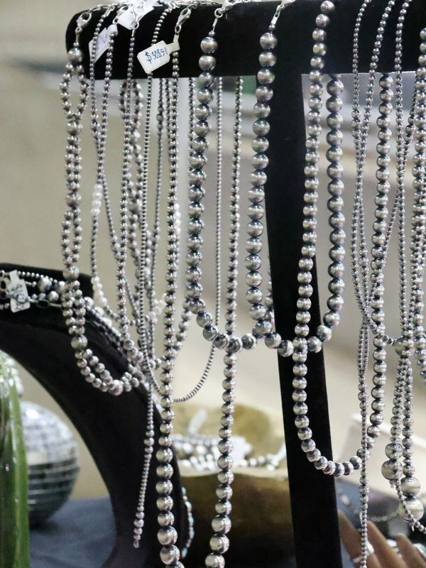 Silver bead necklaces displayed on black jewelry stands.